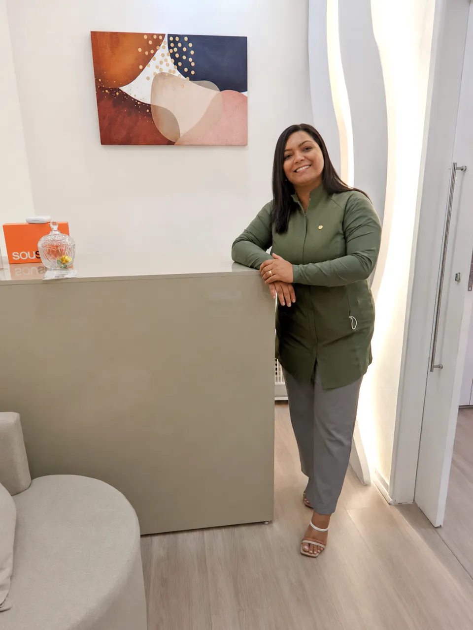 Dra. Juliana Laia sorrindo apoiada no balcão da recepção do seu consultório no Barreiro